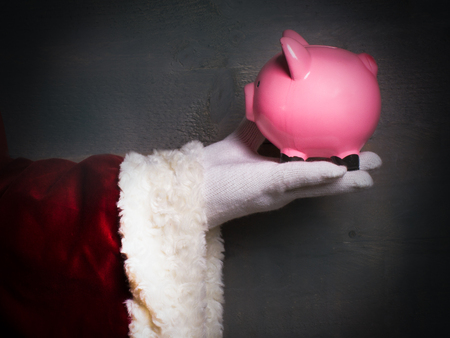 Santa Claus holds a big pink piggy bank on the dark wooden background.の写真素材