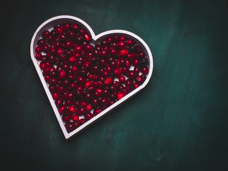 Simple composition with red  berries in a heart shape representing on the blue rough wooden background.の写真素材