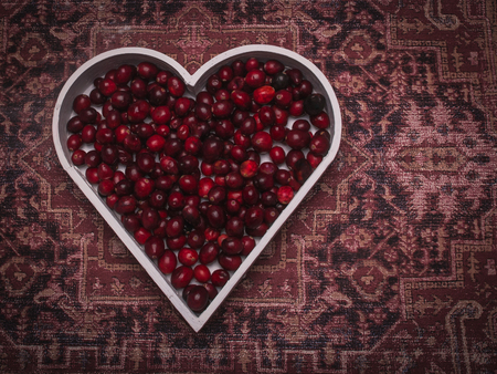 Simple composition with red  berries in a heart shape representing on the textile background with pattern.の写真素材
