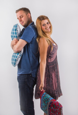 Cheerful young  woman and  serious young man with crossed hands standing back to back with cushions, white background.の写真素材