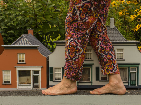 Female legs standing before little houses. Close-up. Ratio, size.の写真素材