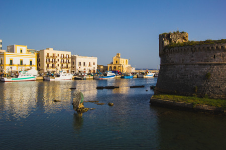 View over boats in the harbor of Otranto to the picturesque old town with old houses blue sky and seawater.の写真素材