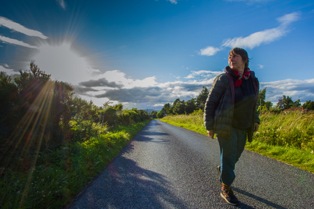 Portrait of one happy senior female walking along the road, in perspective of a way, in a sunny eveningの写真素材
