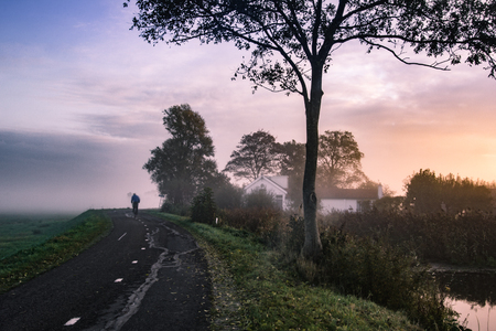 A real life in the province of Friesland Netherlands, a bicyclist rides to work early in the morning.の写真素材