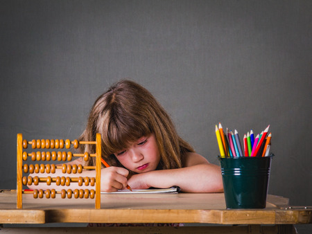Image of capable little girl with colors pencils doing school task in the classroom.