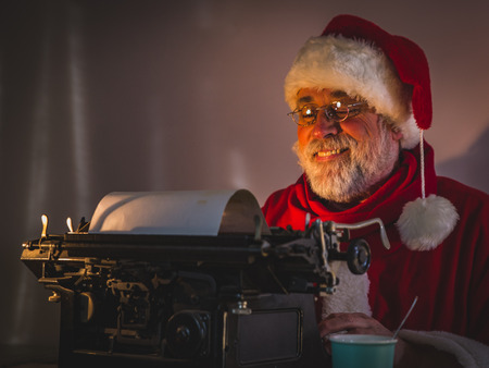 Portrait of happy Santa Claus sitting at his dark cozy room and writing funny message.の写真素材