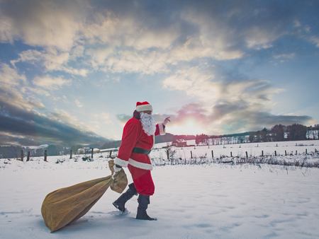 Santa Claus with a large bag of gifts  hurry to the children, winter countryside scenery.の写真素材