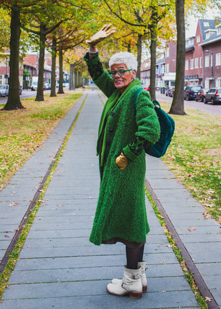Portrait of a senior friendly woman in green coat walking in the autumn alley of the cityの写真素材