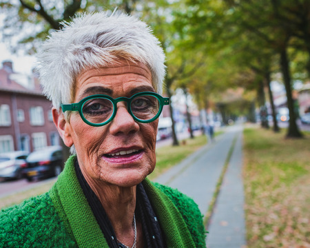 portrait of a senior woman with wrinkles on the skin in the autumn street, outdoor shotの写真素材