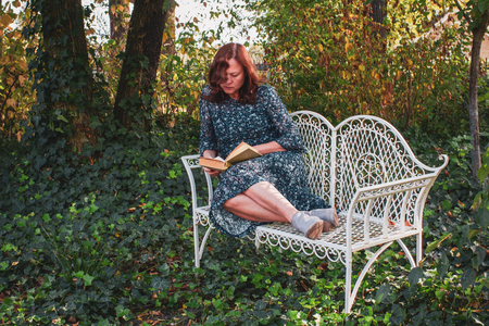Mature woman with a book in her hands sitting in a romantic garden, the beginning of autumn.の写真素材