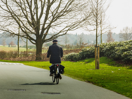 NORTHERN BRABANT - NETHERLANDS - MARCH 26, 2017: old man rides a bicycle in nature park, rear viewのeditorial素材