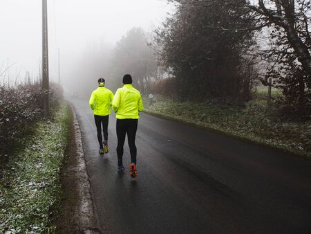 Two athletic young man running in the winter nature.