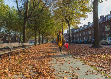 Asian attractive happy trendy senior woman in yellow clothes with red hair walking in autumn alley, perspective view.の写真素材