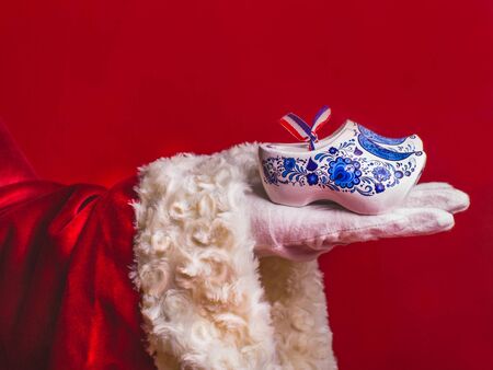 Decorative christmas background with copy space.Typical Dutch wooden clogs in delftsblauw style in hand of  Santa-Claus on a red background, close up.の写真素材