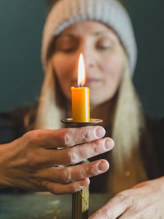 Blonde woman with a burning candle on a dark-green background, view from front, selective focus.