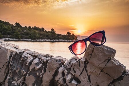 Sunglasses lie on a stone against the backdrop of sunset, bays, mountainsの写真素材