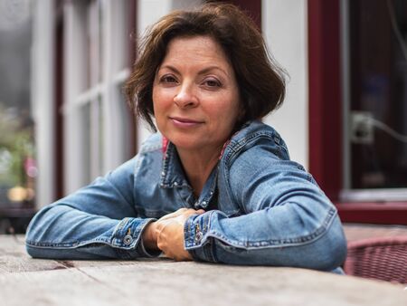 Modern woman of 50-60 years old, in casual clothes, sitting at a table in a cafe on a blurred...