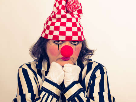 Portrait of a sad clown with a red nose and a hat, in a striped blouse on a white background with copy space.の写真素材
