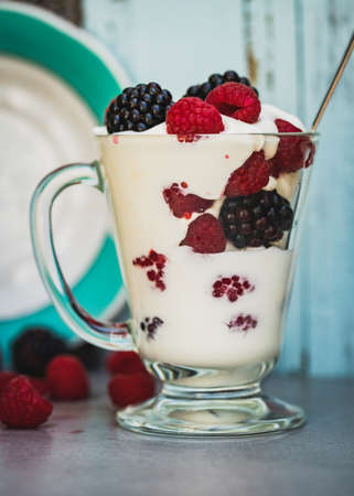 Fresh healthy blueberry and raspberry parfait in a glass on a rustic white wood background and porcelain vintage tableware.の写真素材