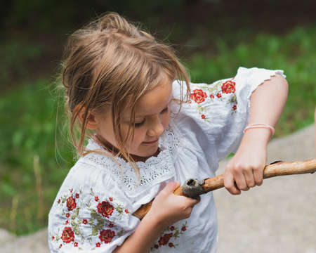 Resourceful dexterous little girl werking with a stick. Fun summertime, provincial life.の写真素材
