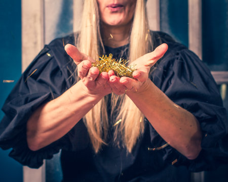 Golden sparkles in hands of woman close-up, hands in focus, model blurred. Cute female blond model of middle age.の写真素材