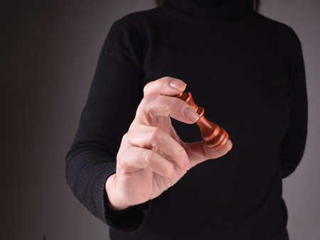 Female hand with Chess Queen on a dark blurred background of woman body in black sweater. Business...