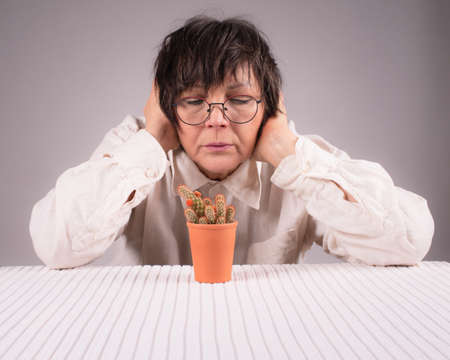A woman of sixty sits at a table and looks at a cactus in a pot.の写真素材