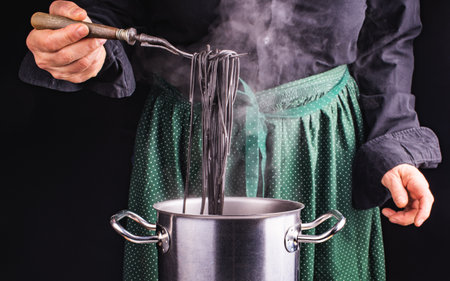 The cook is in the kitchen. Hands of cook and italian black spaghetti on the fork. Background of a green apron with polka dot.の写真素材