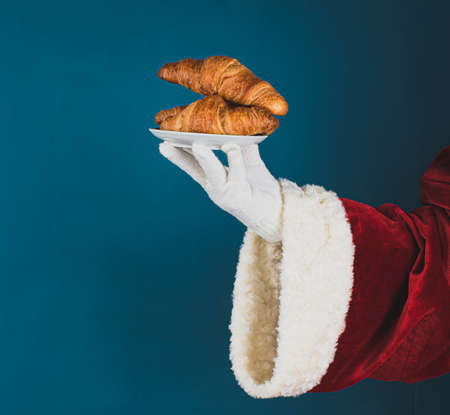 Santa Claus offered croissants. Hand of Santa on a dark turquoise background with copy space.の写真素材