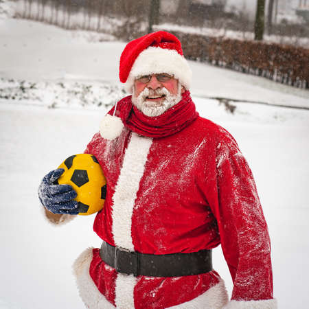 Funny Santa Claus in a traditional costume with a yellow ball playing on a snowy street.の写真素材