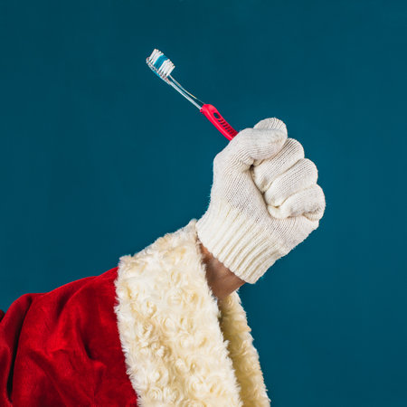 Close-up of Santa Claus's hand in a white glove holds a toothbrush, blue background with copy space.の写真素材