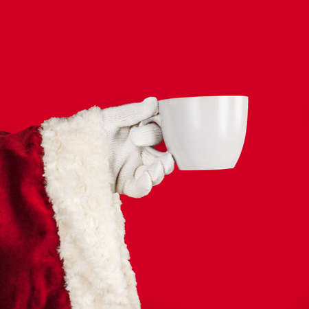 The hand of Santa Claus is holding a white mug. Christmas holiday drink and food concept.の写真素材