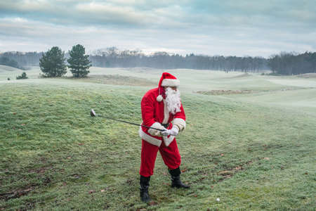 Santa Claus in a traditional red costume plays on the golf course in a beautiful winter early in the morning.の写真素材