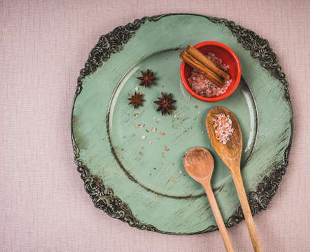 Two wooden spoons with sea salt, star anise, cinnamon sticks on a green plate.の写真素材