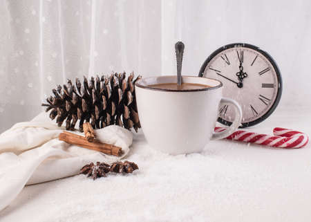 New year concept. The hands on the clock show almost 12 o'clock. A cozy snow-covered white table with a cup of coffee,の写真素材
