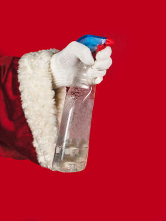 Close-up Santa's hand is holding a plastic bottle, cleaning products on a red background with copy space.の写真素材