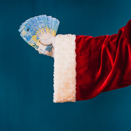 Rich Santa Claus has a lot of money. Santa Claus's hand holds a lot of money, 20 euro banknotes, on a blue background with copy space.の写真素材