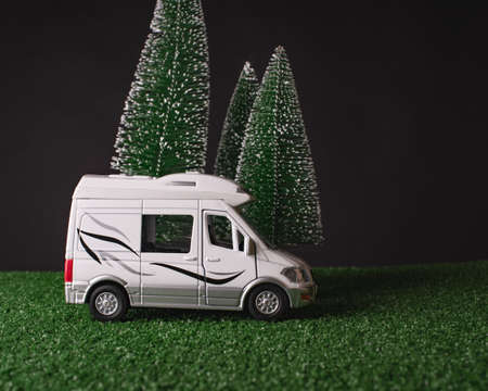 A white camper model stands on green grass and against the background of snow-covered fir trees at night. Christmas night, winter holidays, travel by mobile home.の写真素材