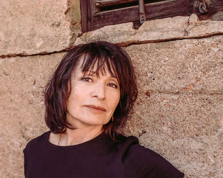 Portrait of mature brunette woman in black shirt by old rough concrete wall with big crack.の写真素材