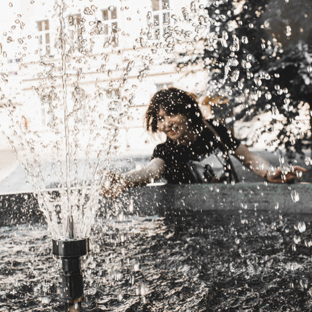 Happy woman by the fountain catches water droplets. Fun moment in warm sunny summer day.の写真素材