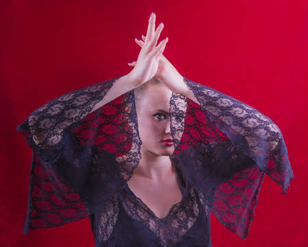 Expression face of an imperious lady in red and black tones, raising her hands up, covering part of her face with a transparent sleeve. Spanish style Carmen, studio shot.の写真素材