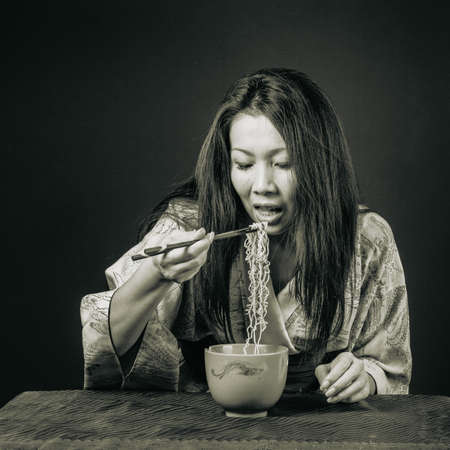 Middle aged Asian woman in kimono eating noodles. Traditional food, clothes and accessories,...