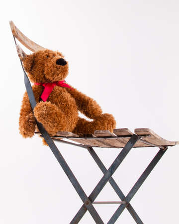 Brown teddy bear with a red ribbon sits on an old chair on a white background with copy space.の写真素材