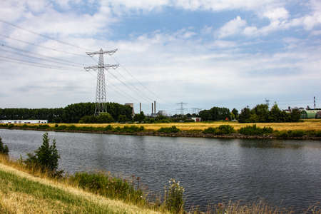 Dutch landscape with a river and high voltage electric poles between trees on yellow grass in the Netherlands.の写真素材