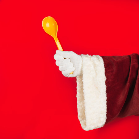 Close up of Santa Claus hand holding a plastic spoon on a red background. Kitchen and cooking concept.の写真素材