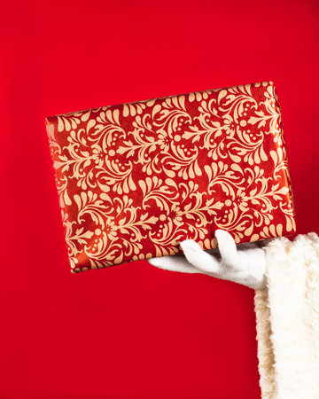 Santa Claus holds a box of gift in his hand on a red background with copy space. Giving a gift concept.の写真素材