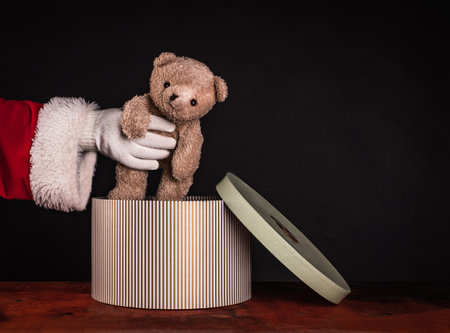 Santa Claus holds soft-toy, brown teddy bear in hand on black background with copy spaceの写真素材