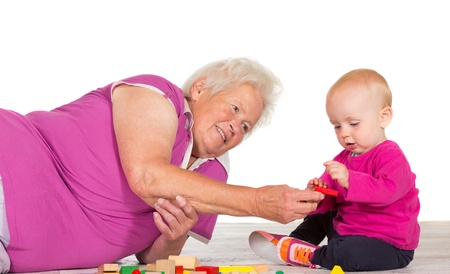 Elderly grandmother lying on the floor babysitting her small grandchild as the two play contentedly together with toy blocksの写真素材