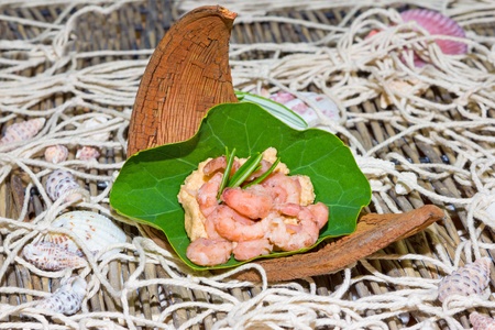 Serving of gourmet shrimps on a fresh green nasturtium leaf garnished with rosemary and served on a wooden deck with a fishing net coveringの写真素材