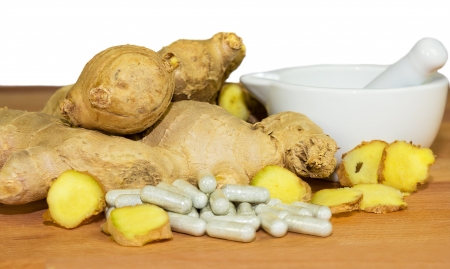 Fresh root ginger with whole and sliced rhizomes alongside a white ceramic pestle and mortar and a...